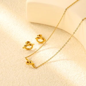 Parure bijoux dorée avec collier à pendentif nœud et boucles d'oreilles sur fond épuré