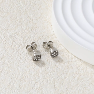 Macro shot of minimalist square cubic zirconia stud earrings on a textured stone surface