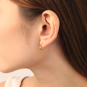 Close-up of golden bamboo texture hoop earring worn on ear with polished finish