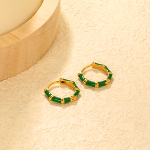 Close-up of bamboo hoop earrings in gold finish with dark green enamel on wooden pedestal