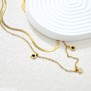 Collier double épaisseur en acier doré avec pendentif étoile sur support texturé blanc