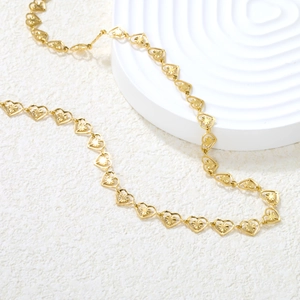 Golden hollow heart chain necklace with detailed radial textures on a white stone pedestal