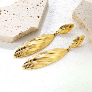 Macro detail of 18k gold plated long striped earrings with leaf shape and metal texture