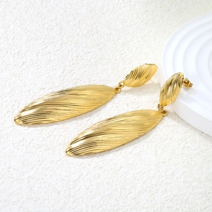 Macro detail of gold-plated leaf earrings with vertical striped texture on stone background