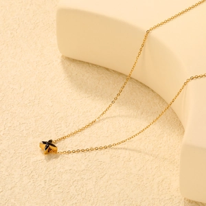 Collier minimaliste en acier inoxydable plaqué or 18K avec pendentif en X sur fond neutre