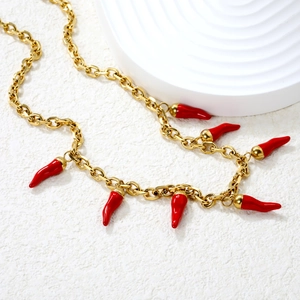 Macro detail of 18k gold chain necklace with vibrant red chili pepper pendants on a white tray
