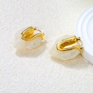 Detail of 18K gold-plated earrings with irregular creamy resin on a stone surface