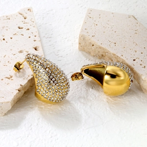 Macro shot of gold teardrop earrings with pavé crystals on a stone surface