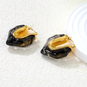 U-shaped gold metal earrings with white marble resin detail on white stone texture