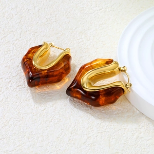 Detail of amber resin hoop earrings with 18K gold plated metal edges on white stone