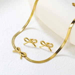 Detail shot of golden bow necklace with matching earrings set on minimalist pedestal
