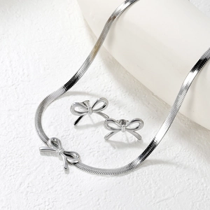 Silver bow jewelry set with snake chain necklace and stud earrings on white display
