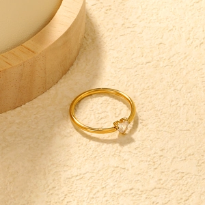 Anello minimalista a cuore dorato con zircone bianco su superficie materica estetica