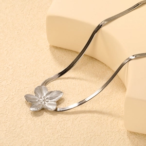 Silver flower pendant necklace with flat snake chain on a geometric jewelry stand