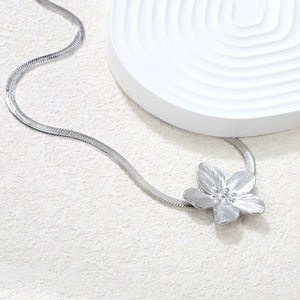 Close-up of silver flower pendant with radial texture on a flat snake bone chain