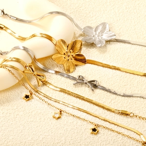 Elegant gold and silver snake chains with petal, bow, and star charms on textured background