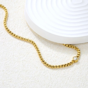 Détail macro d'un collier chaîne box dorée avec pendentif rond en zircon blanc serti