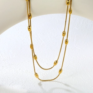 Détail d'un collier chaîne serpent dorée avec perles ovales polies et franges en métal
