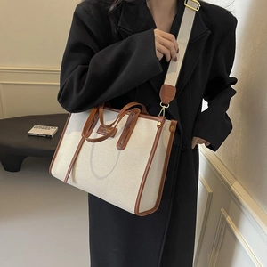Large capacity canvas tote bag with brown leather trim carried by a model in a black coat