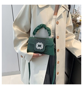 Detail of dark green lizard texture handbag featuring sparkling crystal buckle and pleated handle