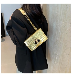 Detail view of gold crocodile embossed crossbody bag with metallic chain and lock
