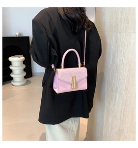 Detail of pink crossbody bag with glitter flap and gold bar lock worn by model