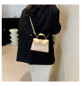Mini bolso trapezoidal dorado con acabado metálico llevado cruzado sobre blazer negro