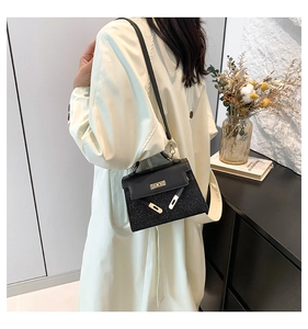 Detalle de bolso bandolera negro con brillo llevado por modelo en un ambiente interior suave