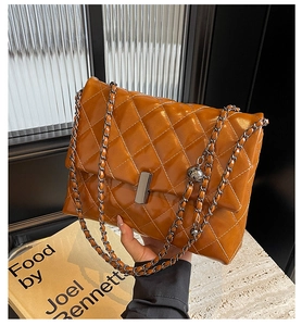 Détail d'un sac matelassé marron avec chaîne dorée et breloque en métal sphérique