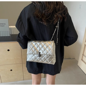 Détail du sac argenté matelassé avec chaîne porté par un mannequin à l'épaule