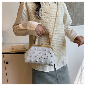 Polka dot handbag with bamboo handle and pearl details worn as a crossbody with chain