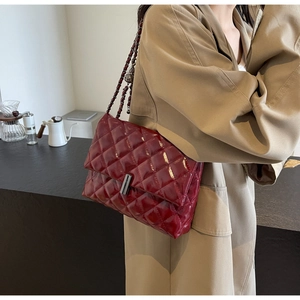 Sac bandoulière bordeaux matelassé en cuir verni avec chaîne sur un trench-coat kaki