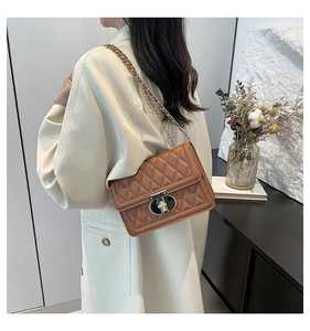 Détail du sac matelassé marron avec fermoir noir et or porté sur un manteau beige