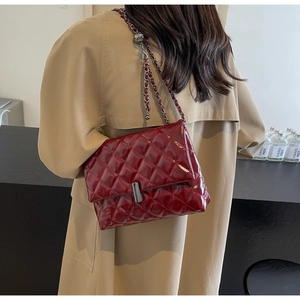 Détail d'un sac à bandoulière matelassé bordeaux en cuir verni avec chaîne dorée chic