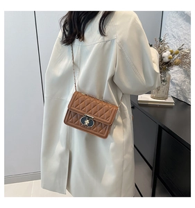 Sac bandoulière marron matelassé avec chaîne dorée porté sur un trench blanc