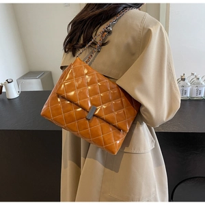 Gros plan du sac chaîne en cuir matelassé marron porté par un mannequin en trench