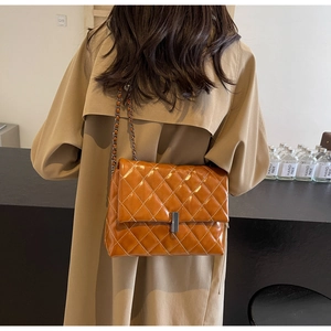 Détail d'un sac bandoulière en cuir marron matelassé avec chaîne sur un trench-coat