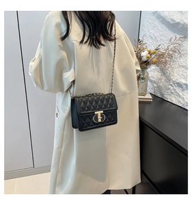 Détail du sac à bandoulière noir matelassé avec fermoir en T doré sur le mannequin