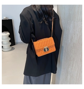 Sac bandoulière orange matelassé avec fermoir doré porté par un mannequin en studio