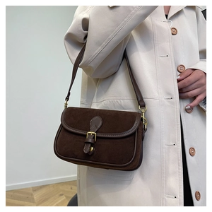 Side view of deep brown suede crossbody bag with vintage buckle on beige trench coat