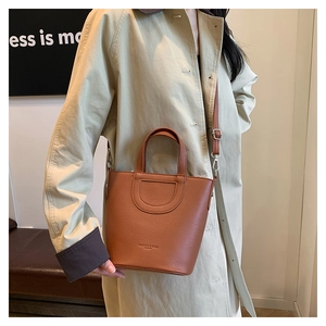 Brown lychee leather bucket bag with D-pocket and adjustable strap worn by a model
