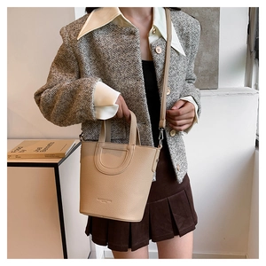 Detail of apricot bucket bag with lychee texture held by a model in a trendy outfit