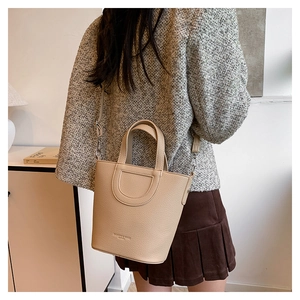Detail of beige bucket bag with lychee texture and dual handles in a minimalist setting