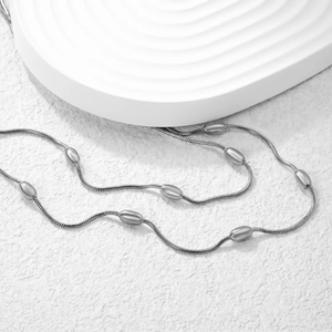 Dettaglio collana a doppia catena serpente argento con perle ovali su superficie in pietra
