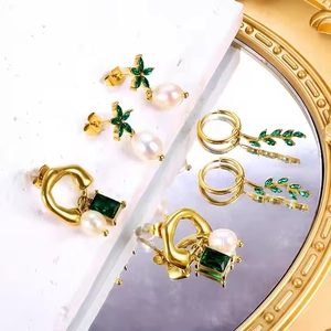 Vintage gold earrings set with emerald green gemstones and pearls displayed on marble