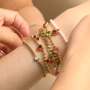 Stack of gold bracelets with colorful heart charms and pearls on model's wrist