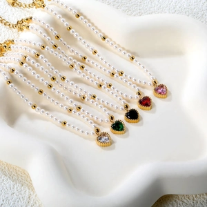 Pearled necklace with multi-colored heart zircon pendants on white wavy jewelry plate