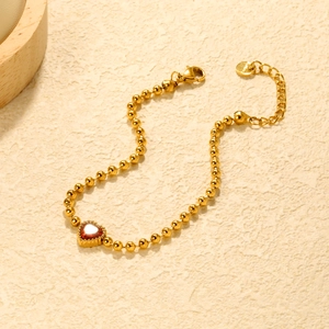 Détail du bracelet à billes dorées avec un pendentif cœur rouge et un fermoir mousqueton