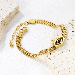 Golden chunky chain bracelet with black evil eye pendant on stone display background