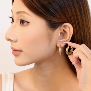 Détail macro des boucles d'oreilles en C plaquées or 18K avec émeraudes et diamants